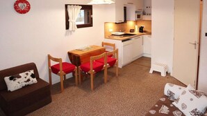 Um espaço compacto para viver, com mesa de jantar, cadeiras, sofá, pequeno espaço de cozinha e porta.