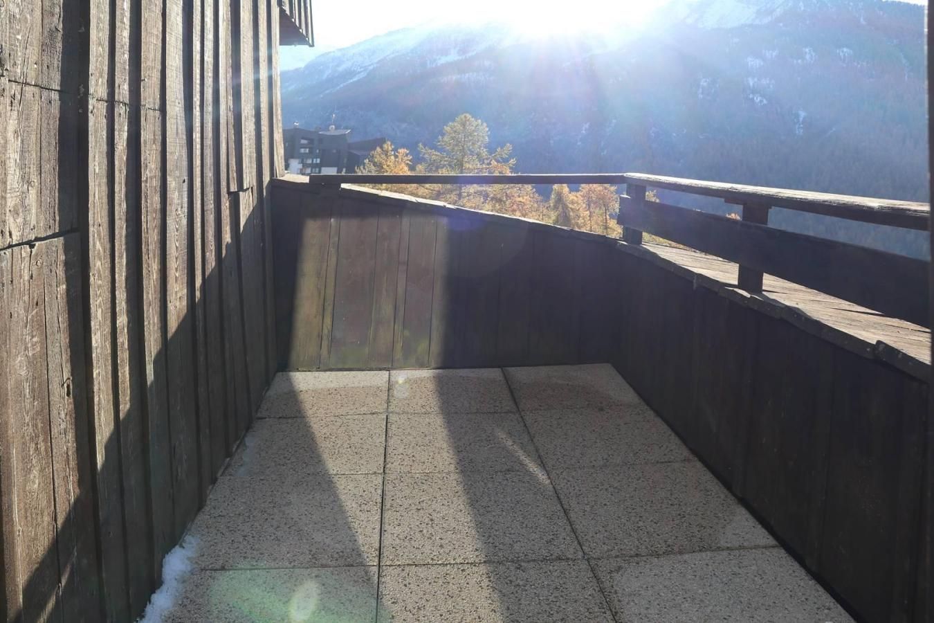 A wooden balcony with a tiled floor, overlooking a mountainous landscape.
