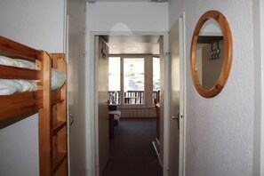 A narrow hallway leading to a room with a wooden bunk bed, a door with a mirror, and a view of a balcony with a railing. - 15m from ski slopes, 5th floor, view resort, balcony, 28m², Les Orres (Les Orres)