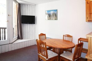 A room with a round wooden table and four chairs, a mounted flat-screen TV, a window with curtains, and a framed picture on the wall. - 15m from ski slopes, 5th floor, view resort, balcony, 28m², Les Orres (Les Orres)