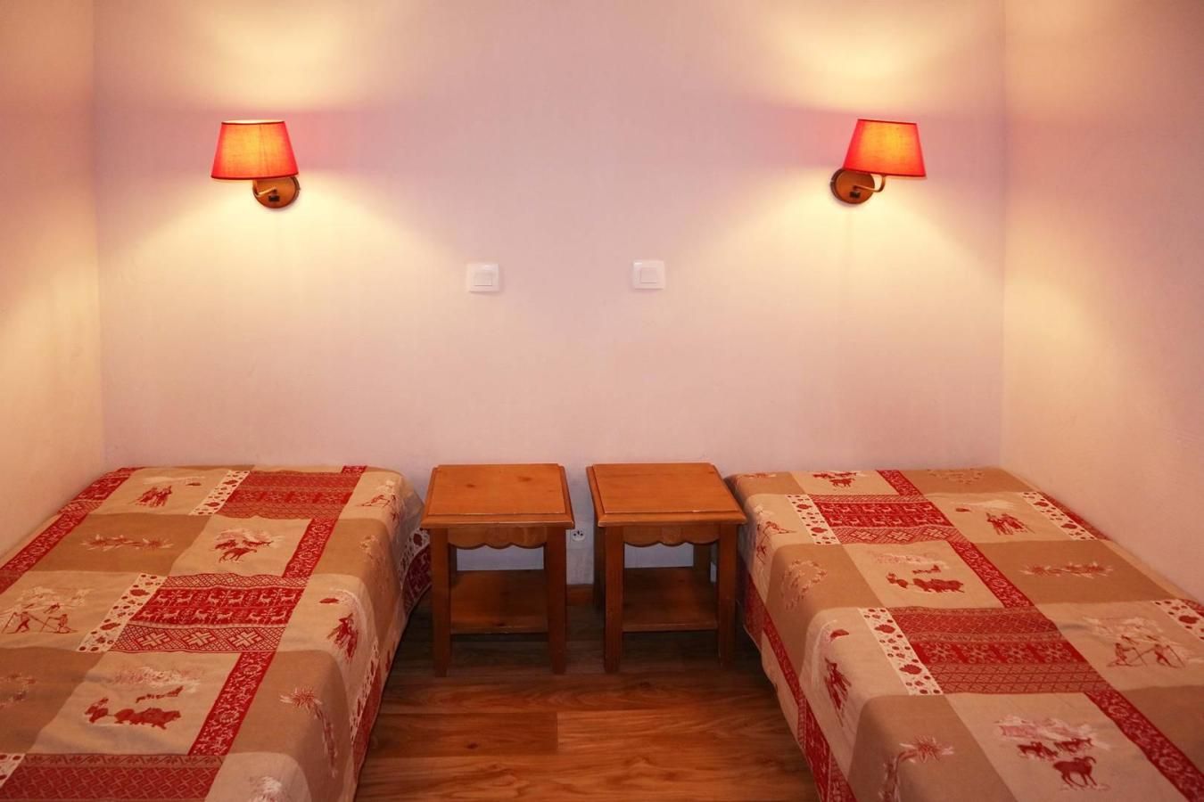 A small room with two beds, a wooden table, and two wall-mounted lamps.