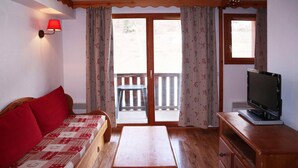 A room with a wooden sofa, a wooden table, a television on a wooden stand, and a sliding glass door leading to an outdoor area.