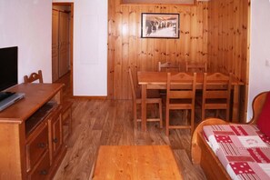 Ein gemütliches Zimmer mit Holzwänden, einem Esstisch mit Stühlen, einem Fernseher und einem Bett mit gemusterten Betttextilien.