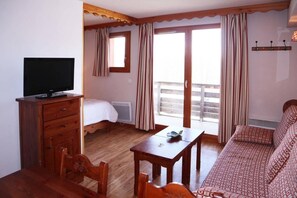 A hotel room with a bed, a TV, a table, a sofa, and a balcony with curtains. - Ski-in/ski-out & foot of the slopes, 1st floor, swimming pool, sauna, balcony, tv, ski locker, 40m² (Les Orres)