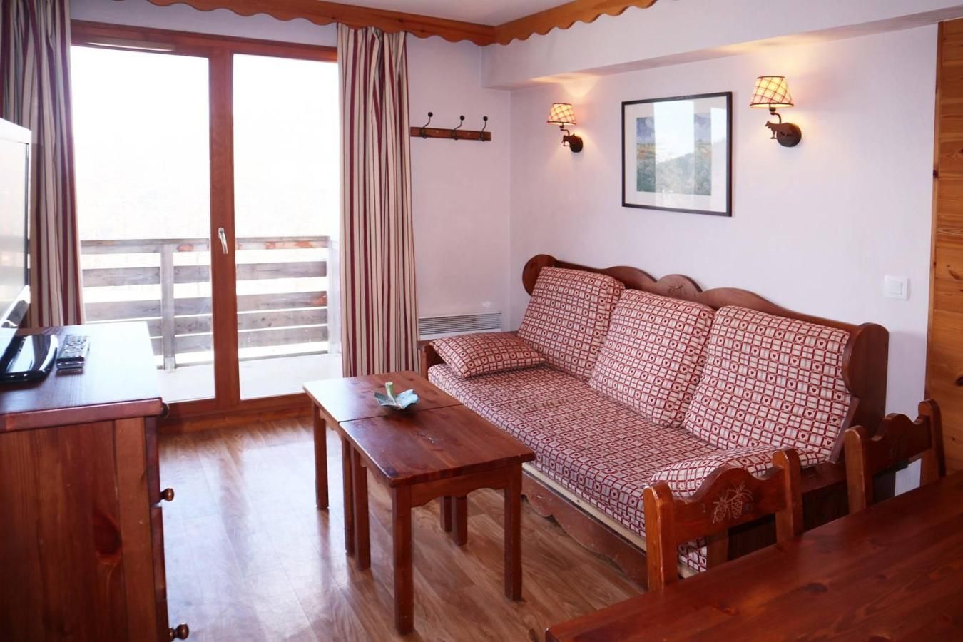 A room with a wooden sofa, a small table, a desk with a telephone, and a window with curtains.