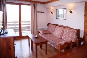 A room with a wooden sofa, a small table, a desk with a telephone, and a window with curtains. - Ski-in/ski-out & foot of the slopes, 1st floor, swimming pool, sauna, balcony, tv, ski locker, 40m² (Les Orres)