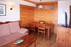 A cozy room with a wooden interior, a sofa, a dining table with chairs, a television on a cabinet, and a lamp. - Ski-in/ski-out & foot of the slopes, 1st floor, swimming pool, sauna, balcony, tv, ski locker, 40m² (Les Orres)