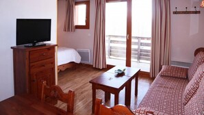 Una habitación de hotel con un escritorio de madera, televisor, cama, sofá y un balcón con cortinas.