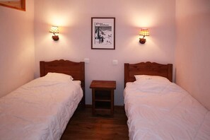 Une chambre avec deux lits simples, une petite table de chevet en bois, deux lampes fixées au mur et un tableau encadré accroché au mur.