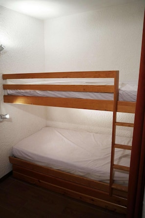 A bunk bed with a wooden frame and white bedding in a room with white walls and a tiled floor.