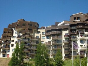 A multi-story residential building with balconies, a sign indicating a pizzeria, and a clear blue sky.
