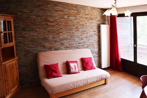 Een kamer met een bakstenen muur, een houten kast, een bank met rode kussens en een raam met rode gordijnen.
