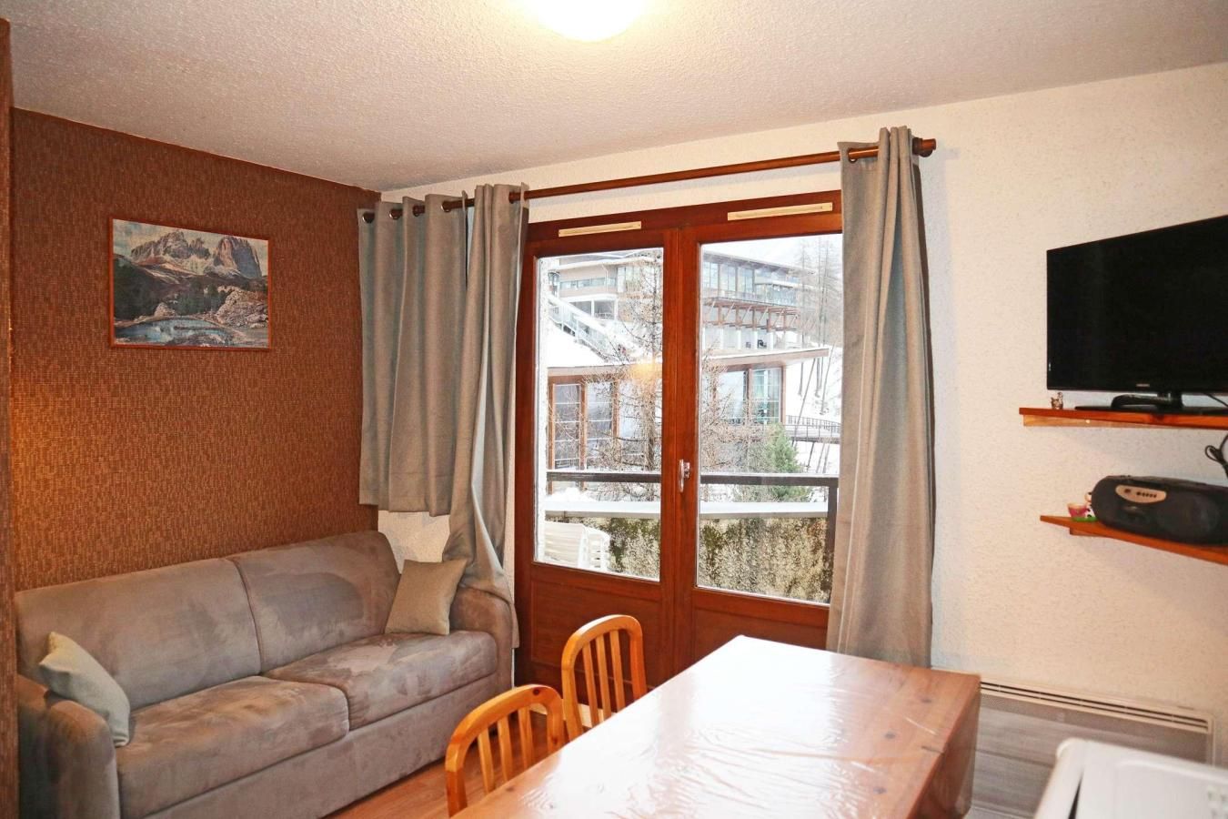 A living room with a sofa, a dining table, a TV, and a window with curtains.