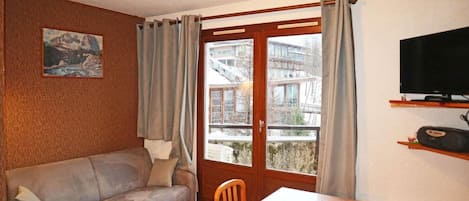 Un salon avec un canapé, une table à manger, un téléviseur et une fenêtre avec des rideaux.
