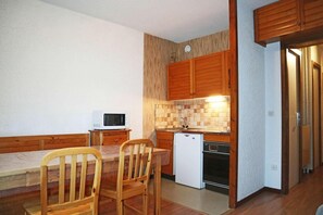 A compact kitchen with wooden cabinets, a microwave, a small refrigerator, and a dining table with chairs.