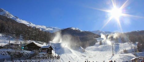 Pista de esquí cubierta de nieve, cielo despejado y sol brillante.