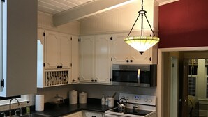 A kitchen with white cabinets, a black countertop, a stainless steel sink, a microwave, an oven, and a hanging light fixture.