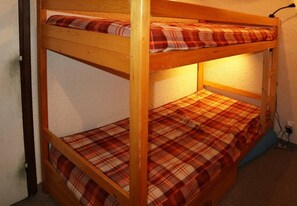 Un lit superposé avec une literie à carreaux et une lampe fixée au mur.