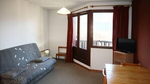 A compact living space with a sofa, a small table, a television, and a window with curtains. - Ski-in/ski-out & foot of the slopes, 7th floor, view valley, balcony, tv, 26m², Les Orres (Les Orres)