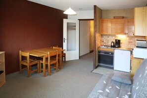 A compact kitchen with a dining area, wooden cabinets, and a small refrigerator.