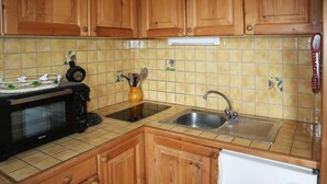 A kitchen with wooden cabinets, a microwave, a sink, and a tiled backsplash. - 15m from ski slopes, 5th floor, view valley, balcony, 22m², Les Orres (Les Orres)