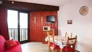 A cozy living room with a red sofa, a dining table with chairs, a TV mounted on a wooden wall, and a wooden ceiling. - 15m from ski slopes, 5th floor, view valley, balcony, 22m², Les Orres (Les Orres)