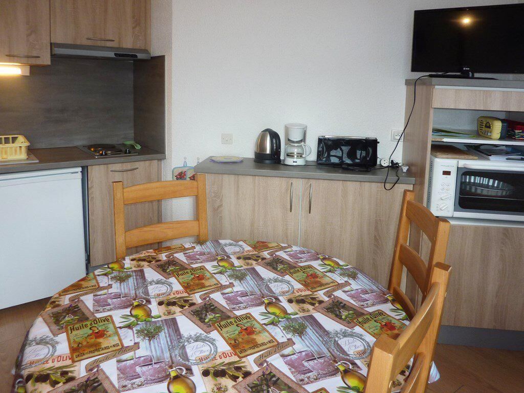 A small kitchen with a table covered in a tablecloth, a coffee maker, a kettle, and a microwave.