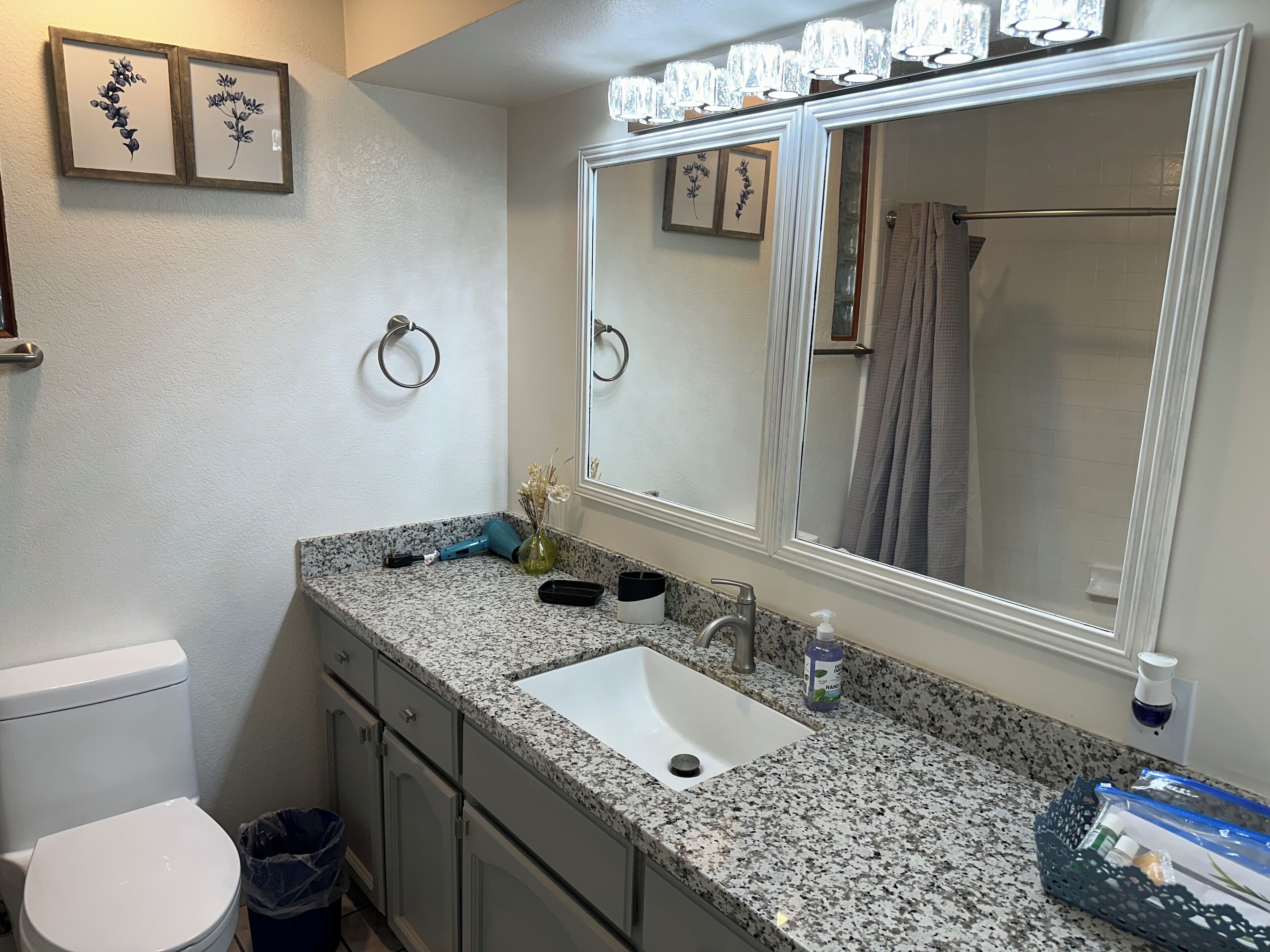 A bathroom with a granite countertop, a white sink, a mirror, and a toilet.
