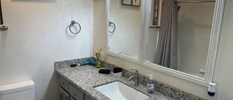 A bathroom with a granite countertop, a white sink, a mirror, and a toilet.