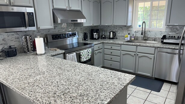 Una cocina moderna con encimeras de granito, electrodomésticos de acero inoxidable y armarios de color gris claro.
