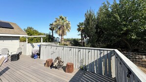 Una terraza de madera con una chimenea, mobiliario exterior y vistas a una palmera y follaje circundante.