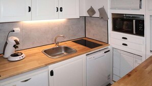 Eine kompakte Küche mit Spüle, Geschirrspüler, Backofen und Kaffeemaschine.