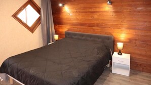 Ein Schlafzimmer mit einem hölzernen Kopfteil, einem Bett mit dunkler Bettdecke, zwei Nachttischlampen und einem Fenster mit Vorhängen.