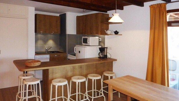 A compact kitchen with wooden cabinets, a microwave, a coffee maker, and a wooden dining table with bar stools.