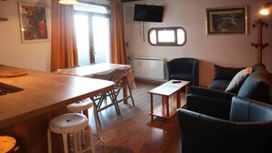 A cozy living area with a wooden dining table, bar stools, a sofa, and a television mounted on the wall.