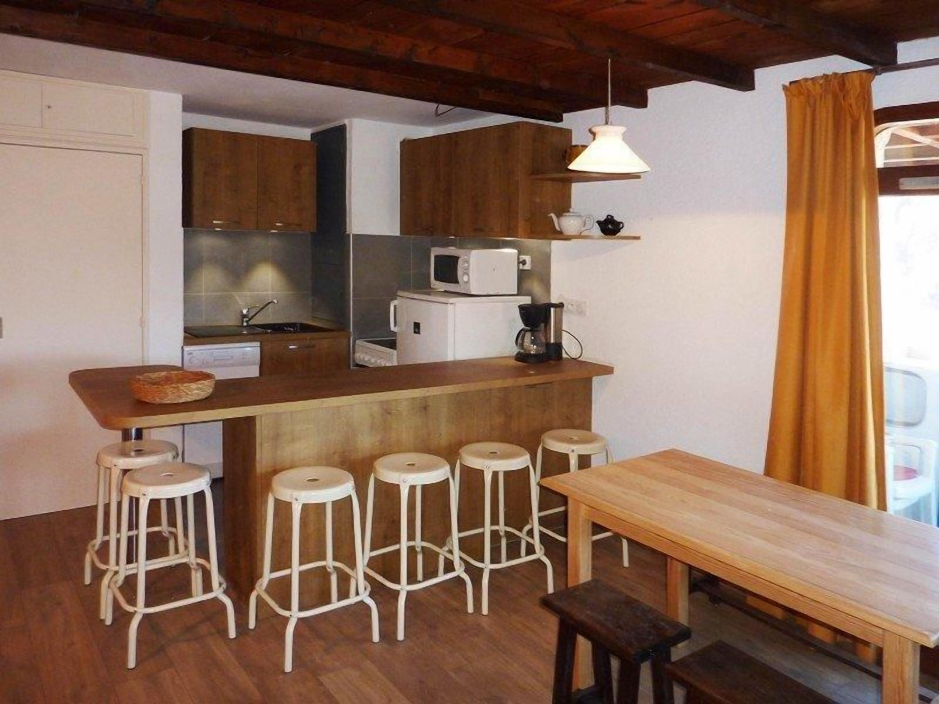 A compact kitchen with a wooden countertop, white stools, and a wooden table.