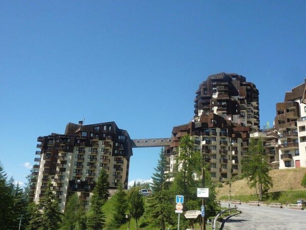 A multi-story residential building with balconies, a pedestrian bridge, and a clear sky.