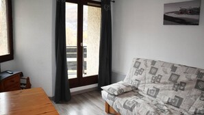 Een kamer met een houten tafel, een gestreept bankstel, een schuifpui en een ingelijst schilderij aan de muur.