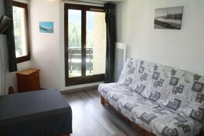 A room with a sofa, a small wooden table, a window with a view of greenery, and a picture on the wall.