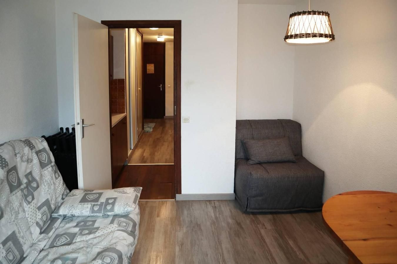 A compact living space with a sofa, a chair, a wooden table, and a hanging light fixture.