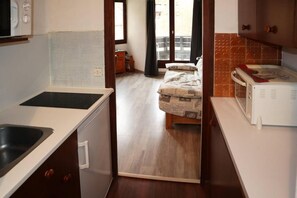 A compact kitchen with a sink, stove, and microwave. A bed with patterned bedding is visible through an open doorway. - 50m from ski slopes, 4th floor, balcony, 26m², Les Orres (Les Orres)