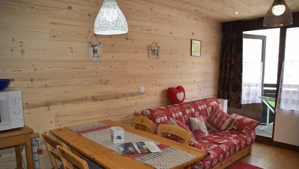 A cozy room with a wooden wall, a red patterned sofa, a wooden dining table with chairs, and a hanging pendant light. - 150m from resort center, 1st floor, balcony, parking, tv, ski locker, 26m², Montgenèvre (Montgenèvre)