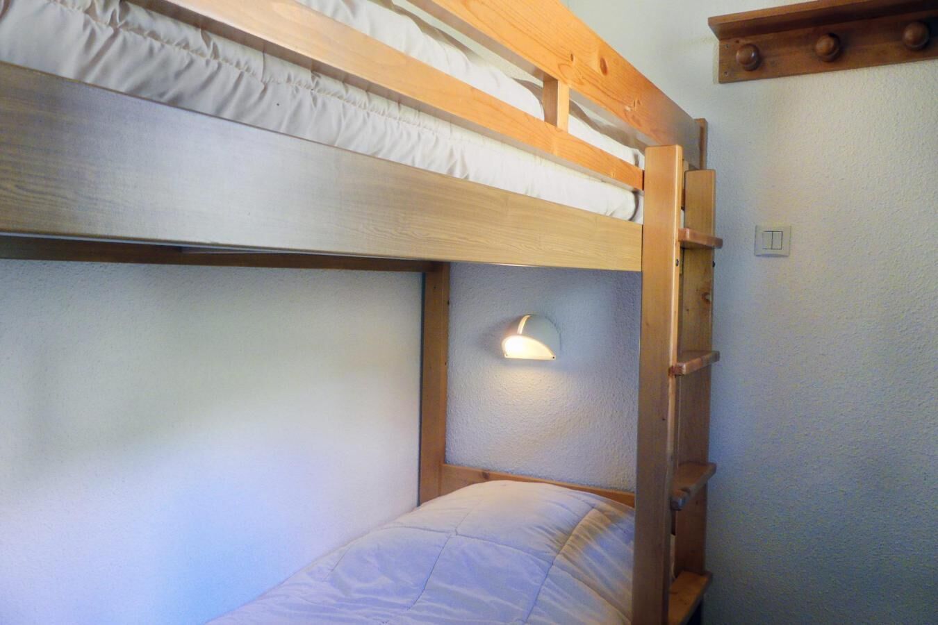 Un lit superposé avec une structure en bois et une seule applique murale.
