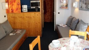 Una habitación compacta con un separador de madera, una pequeña mesa con mantel blanco y un sofá con cojines grises.