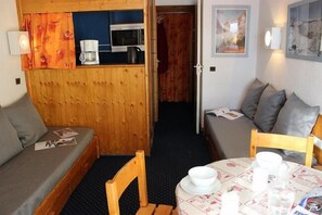 A compact room with a wooden partition, a small table with a white tablecloth, and a sofa with grey cushions.