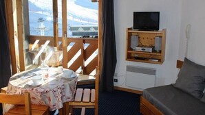 Una habitación con una cama, un televisor en un estante de madera, una mesa con mantel y vistas a un paisaje nevado a través de un ventanal.