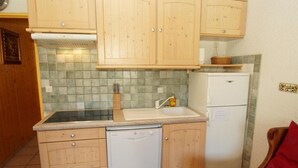 Een compacte keuken met houten kastjes, een vaatwasser, een koelkast en een betegelde spatwand.