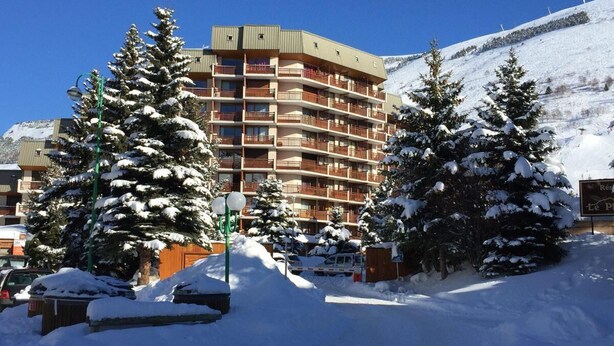 Een meerlaags hotel met balkons, omringd door met sneeuw bedekte bomen en een berg op de achtergrond.
