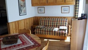 Ein gemütliches Zimmer mit einem karierten Sofa, einem Holzschrank und einem Esstisch mit einem gemusterten Tischläufer.