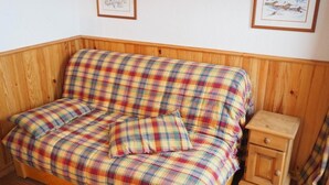 Ein Holzsofa mit kariertem Bezug, ein Holznachttisch und zwei gerahmte Bilder an der Wand.